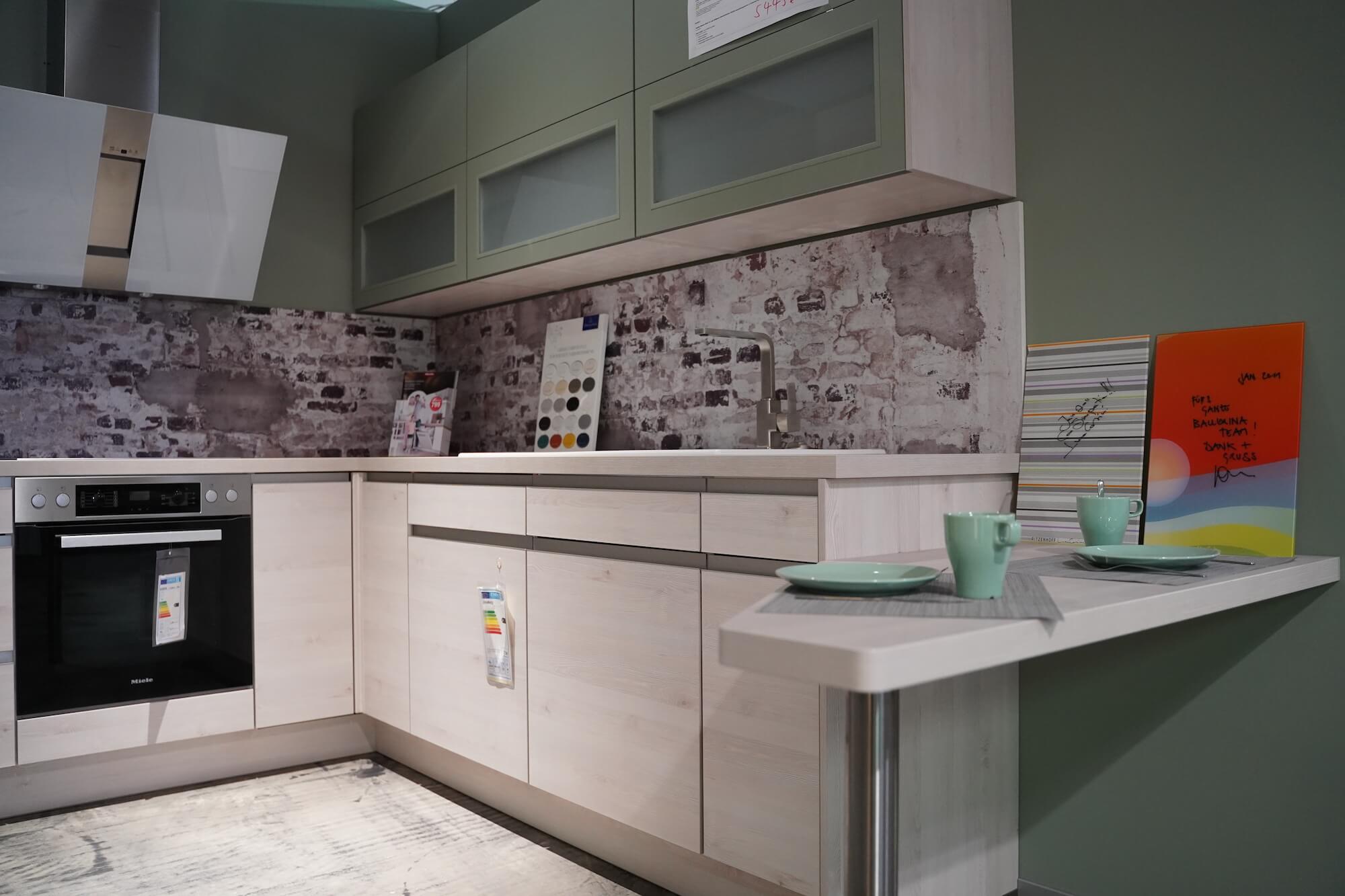 Nobilia Riva Design U-Küche helle Holzfronten und Griffmulden mit grünem Hängeschrank